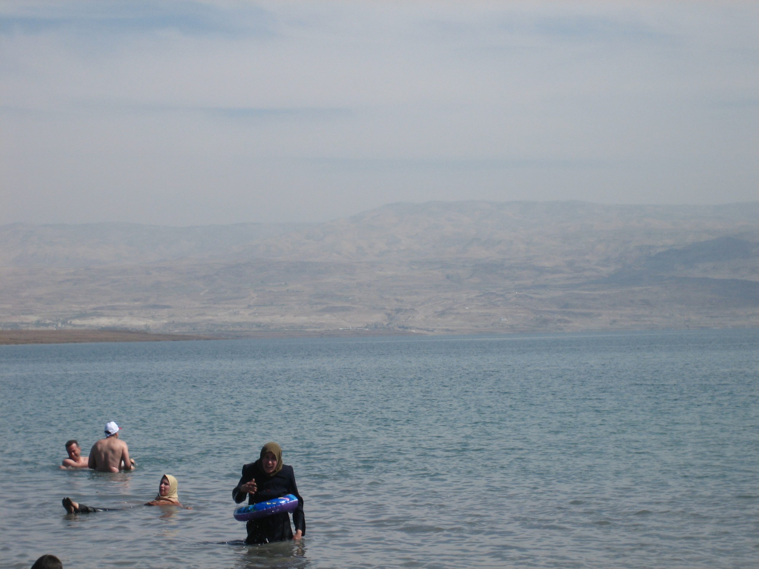 A visitor floating effortlessly on their back in the Dead Sea with the salt-crusted shoreline behind