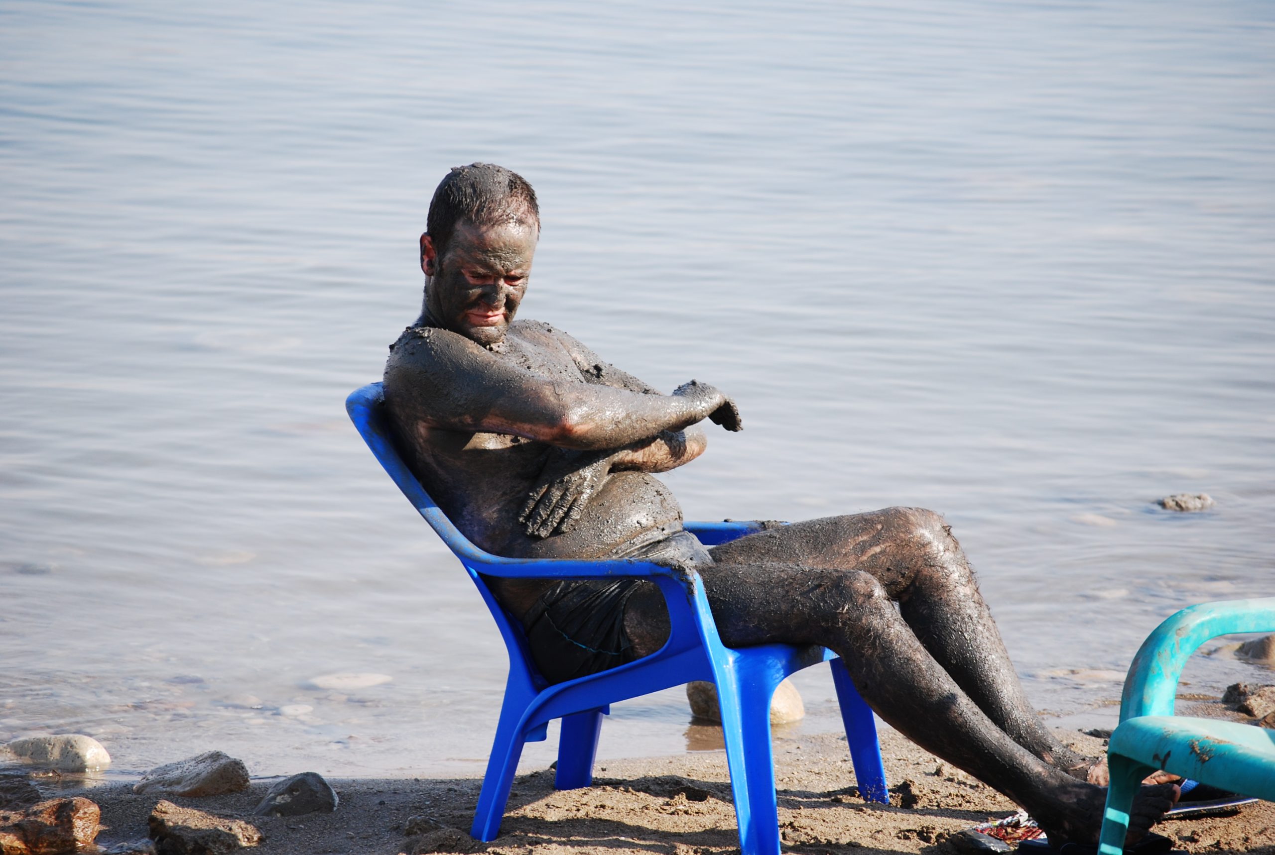 A man applying black Dead Sea mud to his arm on the beach