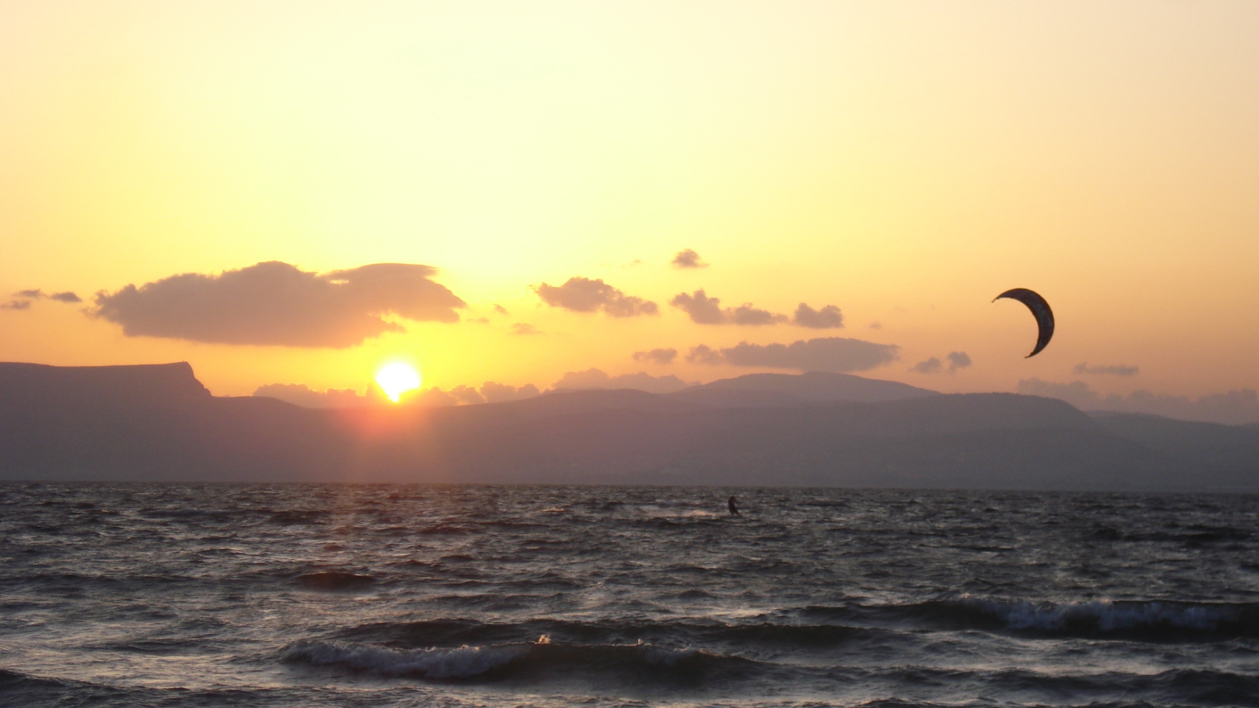 Sunset over the calm water of the Sea of Galilee in Israel, with still reflections and distant hills